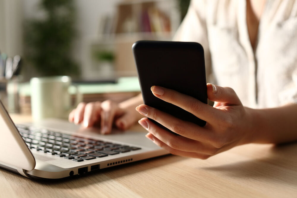 Close up of woman hands using laptop checking smart phone