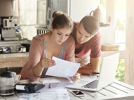 Two people with papers sitting in front of a laptop