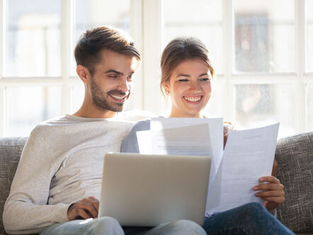 Smiling couple sit on couch using laptop taking care of utility bills 