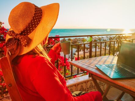 Woman sitting on a balcony in front of a laptop in the sun